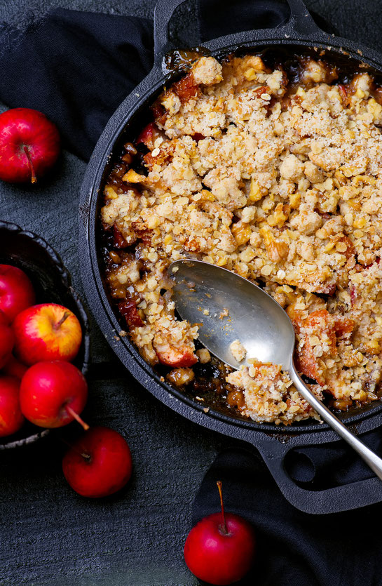 Apfel Crumble mit roten Äpfeln in schwarzer Auflaufform auf schwarzem Untergrund