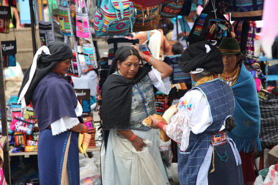 Some indigenious woman who are bargaining for two guinea pigs on the market.