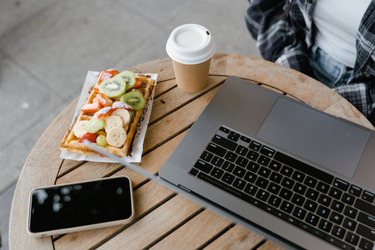 木目調のデスクのうえ。コーヒーの入ったカップ&ソーサ。黄色の表紙の書籍。ノートパソコン。
