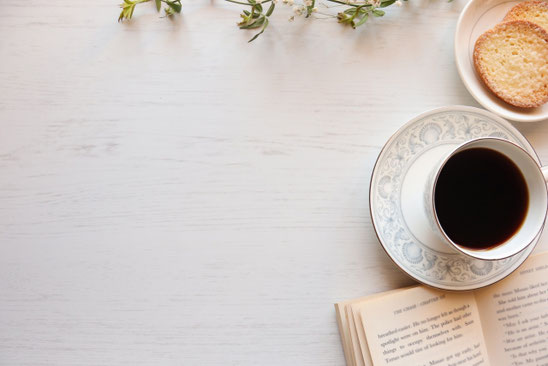 コーヒーの入ったカップ&ソーサ。ラスクがのったお皿。ページがめくられた本。