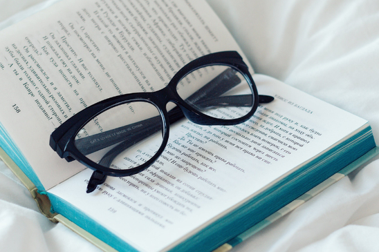 ベッドの上に置かれた本。開かれたページの上に置かれた黒ぶち眼鏡。