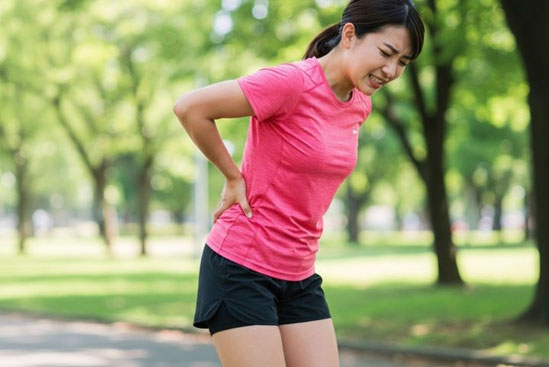 ランニング中に腰を押さえて痛みに顔をしかめる女性