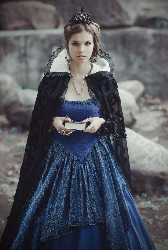 A woman in an elegant blue gown with a royal black cape, adorned with intricate lace and a tiara.