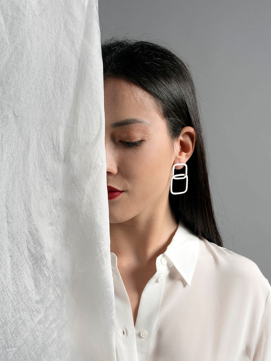 jeune fille portant une grande boucle d'oreilles en argent composée de deux carrés  cachée à moitié par un voile blanc