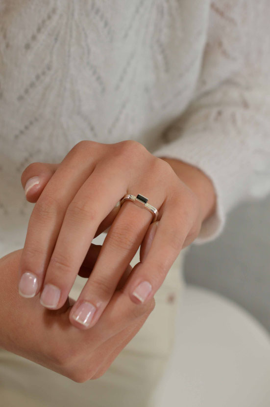 main de femme qui porte une bague carrée en or blanc sertie d'une tourmaline baguette