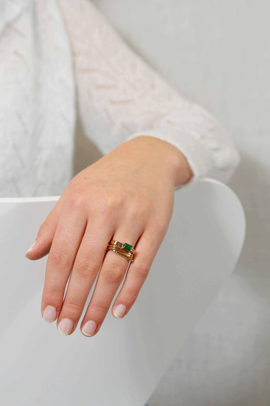 Main de femme portant une bague carrée en or rose 18 carats recyclé sertie d'une émeraude taille baguette