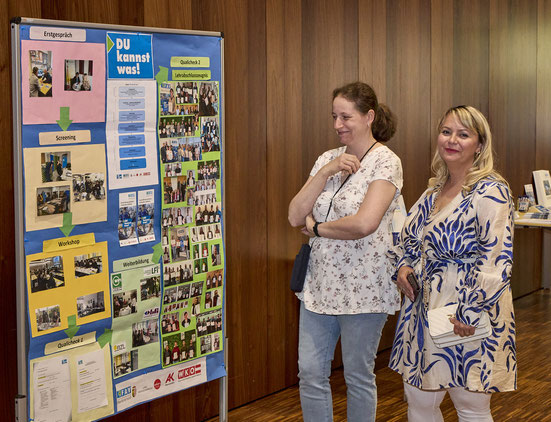 Zwei Besucherinnen betrachten aufmerksam eine Projektwand mit Fotos