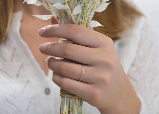 main de femme qui tient un bouquet de mariée en fleurs séchées et qui porte une alliance martelée en fil carré 1.5mm en or blanc palladié 18 carats