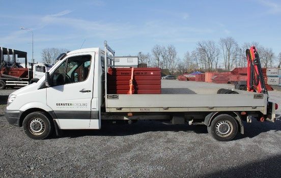 Ein weisser Lieferwagen von Gerster Recycling mit Mulde, Container, Box. Im Hintergrund sind mehrere grosse rote Abfallcontainer mit dem Logo von Gerster Recycling zu sehen. Das Bild zeigt einen Recycling- und Abfallentsorgungsbetrieb und Kleintransporter