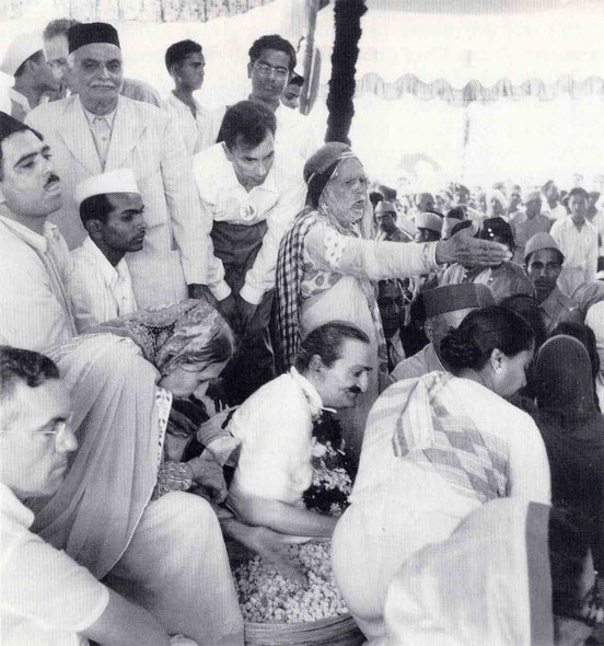 September 1954, Ahmednagar, India : Meher Baba giving prasad to the passing crowd of followers, Maharaj standing next to Baba & instructing. Image courtesy of Lord Meher p.4429.