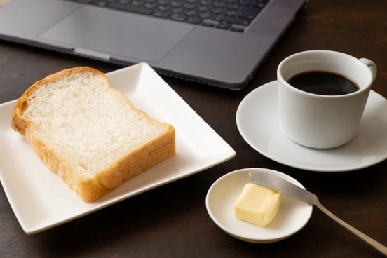 カフェのテーブルに広げられたノートパソコン。パンとバターのお皿。コーヒーの入ったカップ&ソーサ。
