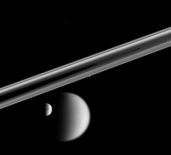 Vier Saturnmonde: Titan (hinten), Dione (vor Titan), Prometheus (Mitte, unter den Ringen) und Telesto (oben) mit Saturnringen im Mittelgrund; fotografiert von der Raumsonde Cassini