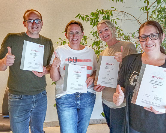 Vier Absolvent:innen bei Gruppenfoto mit Urkunden