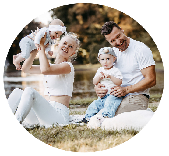 Eine glückliche Familie im Schlossgarten in Teutschenthal. Die Mutter hebt lachend ihr Baby in die Luft, während der Vater das ältere Kind liebevoll auf den Schoß hält. Neben ihnen liegt ihre treuer Vierbeiner. 