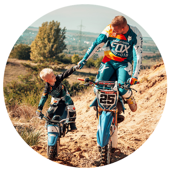 Der Vater balanciert sein Bike auf dem Vorderrad, während sein Sohn ihn mit strahlenden Augen auf seiner eigenen Maschine begleitet. Beide in voller MX-Ausrüstung, umgeben von staubiger Action im Mansfelder Land.