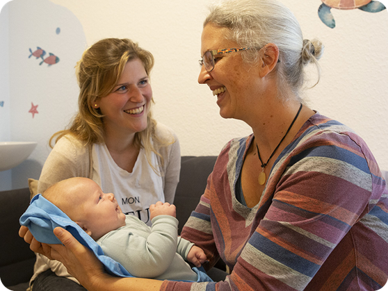 Christiane Merklein in der Hebammensprechstunde mit einer Mutter und deren Baby auf dem Arm