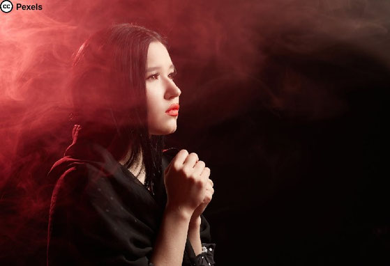 Eine junge Frau scheint zu beten. Rotes Licht und Rauchschwaden. Foto von Mikhail Nilov auf Pexels.