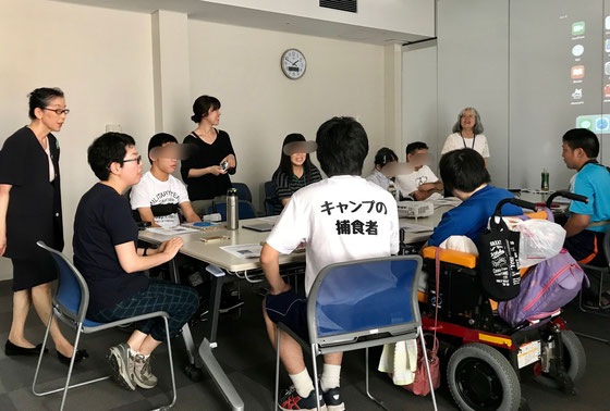 ☆只今13:50。いよいよはじまりました。案内役の佐藤弥子さん(右から二番目の女性)が自己紹介中。左が立っている生田美子さんの右隣り黒の洋服メガネの女性が今回のご担当者様。その右隣りのTシャツ(背中に「キャンプの捕食者」)の男性が高校生サポーター。