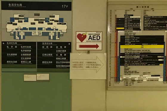 ☆都庁生活文化部。NPO法人の届出窓口の案内板が「AED」の矢印の下に張り紙。