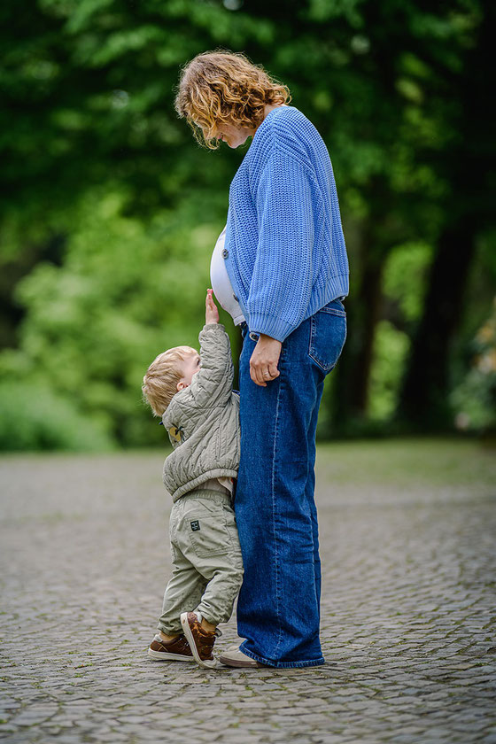 Kleiner Junge streckt sich, um den Babybauch seiner Mutter zu berühren.