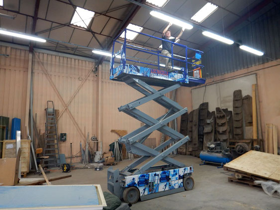 Thierry Besançon entrain d'installer un éclairage LED au plafond dans un atelier professionnel