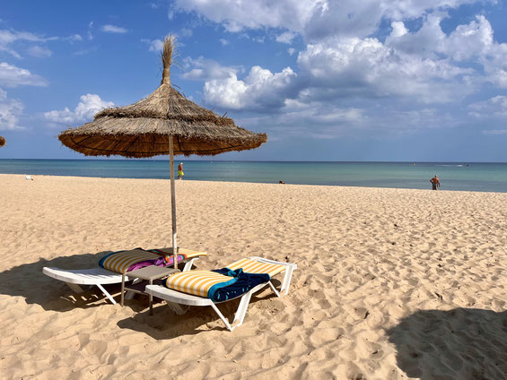 lettini e ombrellone di paglia su spiaggia dorata di Hammamet e mare sullo sfondo