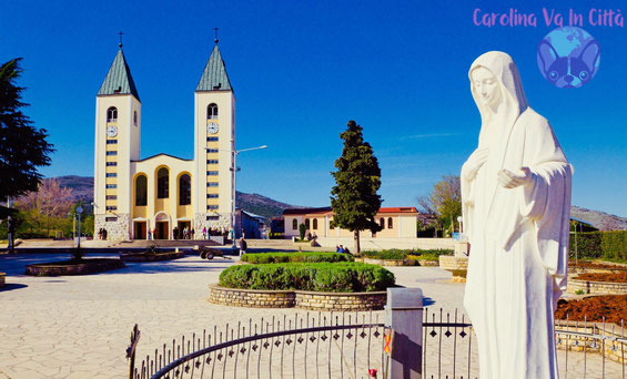 Piazza principale di Medjugorje con statua della Madonna e chiesa con due campanili gialli