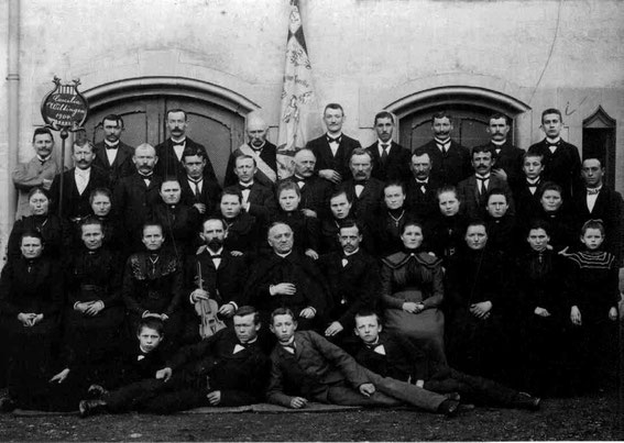 Der Kirchenchor im Jahre 1904 mit der Vereinsfahne. Herr Caspar mit Violine, rechts daneben Pfarrer Joseph Dehen (Dienstzeit: 1902-1924, Erbauer der Pfarrkirche), Chorleiter Herr Göbel (oben links).