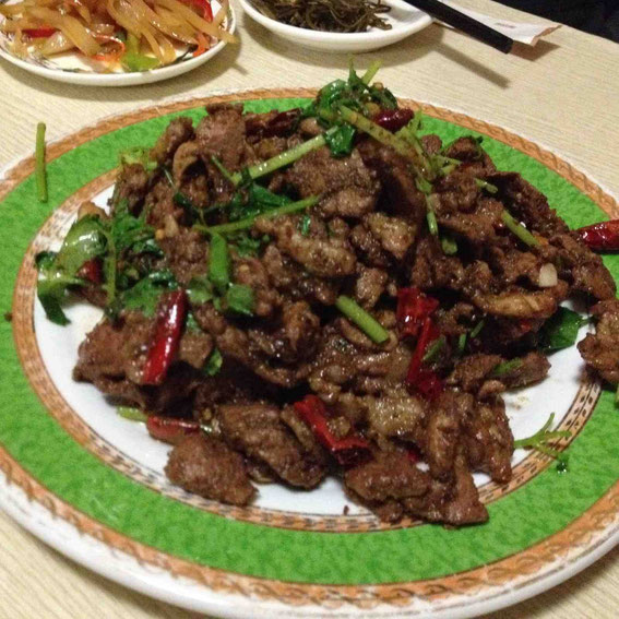 孜然羊肉(羊のクミン炒め)。後ろに見えるのは沙葱の和えもの、地元の野菜の漬け物の和えもの
