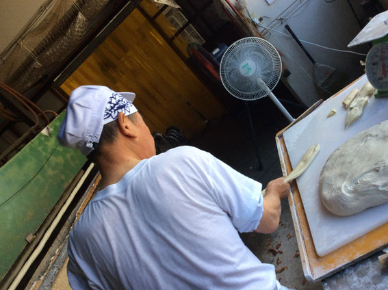 80代の職人さん。グルテンを均等に伸ばして芯の上に巻いていく。日に2000本を焼く。