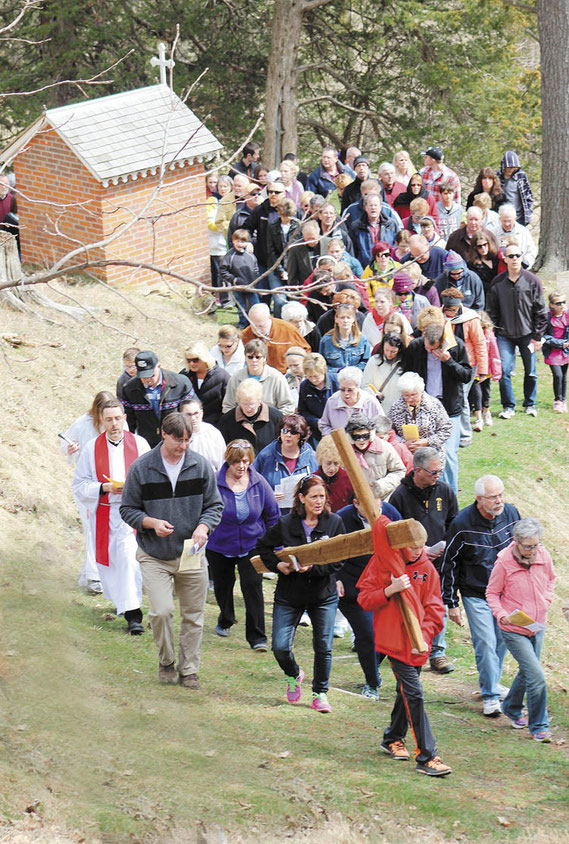 Hundreds attended the Outdoor Way of the Cross service in St. Donatus on Good Friday. Above, the cross is carried past the stations to the old Chapel on the bluff overlooking the church and the community.