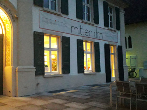 Foto des Eingangs des Cafés "mitten drin" in Schriesheim. Die Fenster sind hell erleuchtet. 