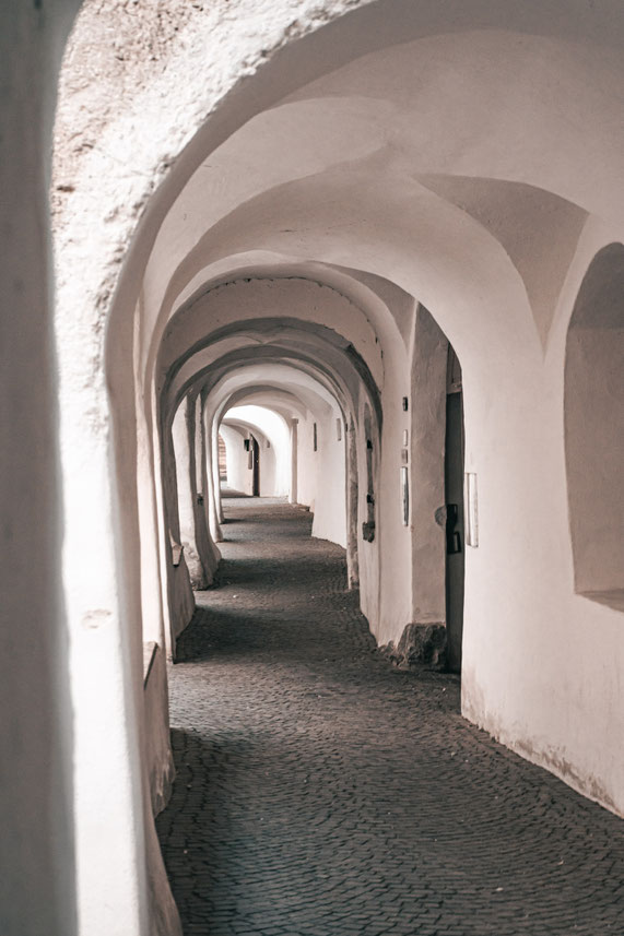 A vaulted historic passageway with white arches and a cobbled floor.