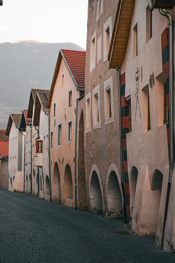 Schmale historische Gasse mit Arkadenhäusern und roten Ziegeldächern.