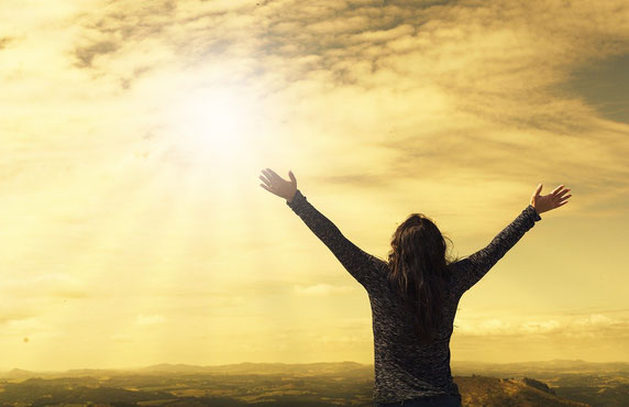 Femme brune qui écarte les bras au ciel. Le ciel est doré.