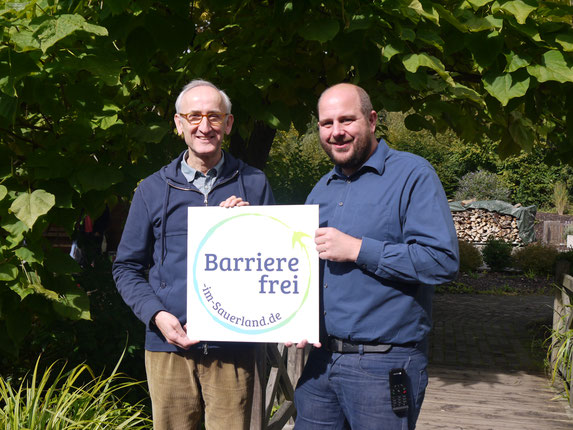 Marc Brüggemann (r.) und Bernhard Pilgram mit dem Signet von „Barrierefrei im Sauerland“.