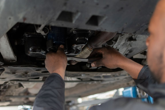 Cette image représente un technicien qui interviens sur un véhicule automobile. Le technicien à un cliquet dans ses mains et est en train de deviser un filtre.