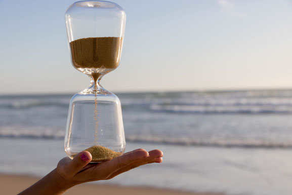 Sanduhr auf Hand vor Meer mit wenig Sand unten im Glas.