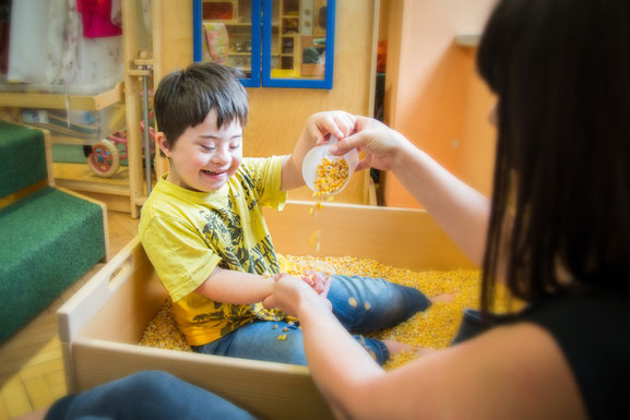 bub-down-syndrom-betreuerin-vinco-heilpädagogischer-kindergarten-maiskorn-spielen