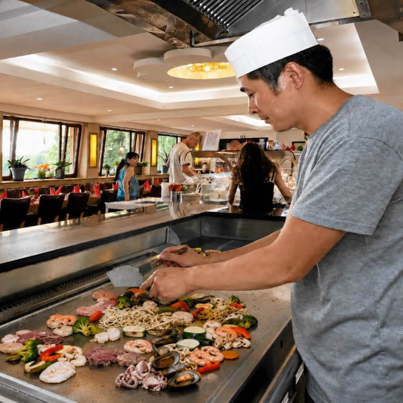 Koch grillt Fleisch, Garnelen, Muscheln und Gemüse auf der Teppanyaki-Platte