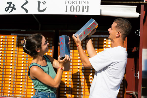 Couple playfully  drawing omikuji fortune slips at a temple in Tokyo — fun and candid cultural photo experience in Asakusa
