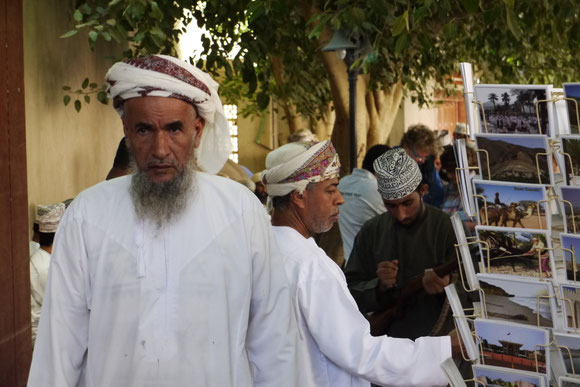 der Oman im Umbruch: der ältere Mann neben einem Postkartenständer, der auch die alten Zeiten zeigt, für die Touristen, mit denen neue Strukturen geschaffen und neue Lebensformen Einzug halten