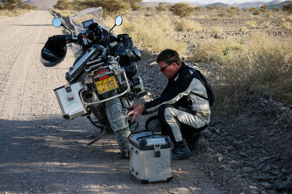 Im Schatten einer anderen Akazie stehend, kontrolliert Jan die Kabelbinder, mit denen wir diesmal verhindern wollen/werden, dass der Schmutzfänger abvibriert wie auf der ruta 40 in Argentinien.