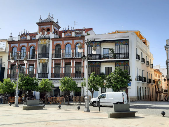 2 schöne Häuser an der Plaza de España. Davor saßen Leute in den Bars. 