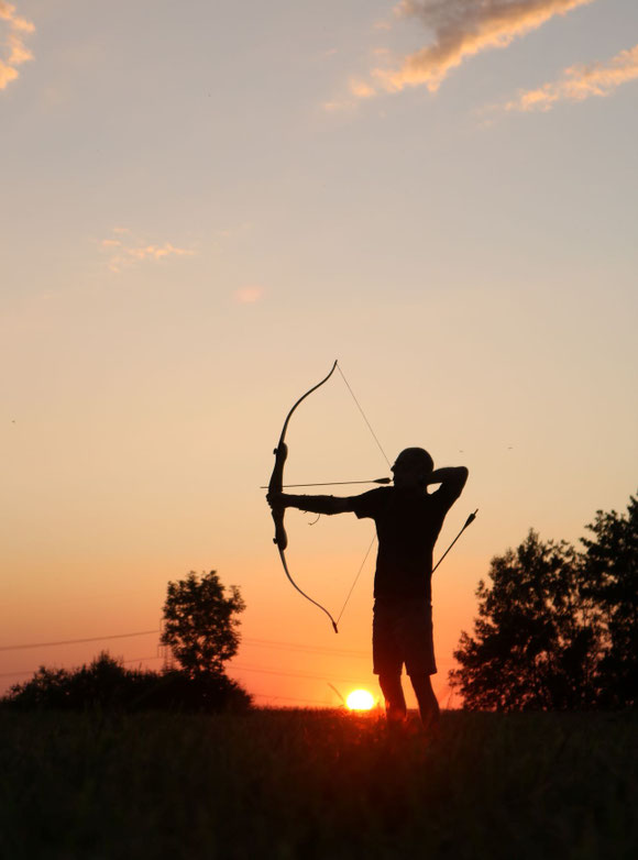 Ein Mann bei Naturnah Bogenschiessen beim intuitiven Bogenschiessen bei Sonnenuntergang um Entspannung und Achtsamkeit zu finden.