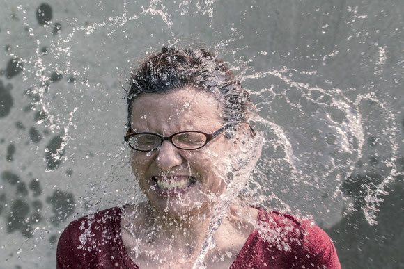 Frau mit Brille bekommt sehr viel Wasser ins Gesicht