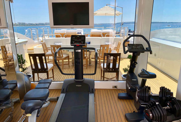 Salle de sport privée de luxe à bord d’un yacht à Monaco, équipée d’un tapis de course, de poids et offrant une vue panoramique sur la mer pour des séances de coaching haut de gamme.