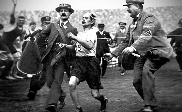 Dorando Pietri siendo ayudado por un oficial para cruzar la línea de meta del maratón de Londres 1908