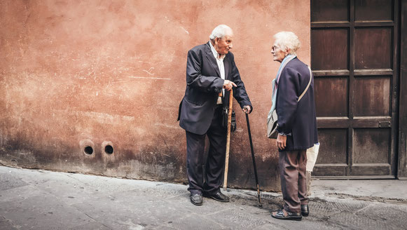 un homme âgé avec deux cannes discute avec une dame de son âge près d'une porte marron