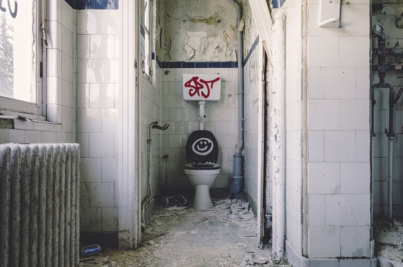 Des toilettes abandonnées et sales, pleines de papiers par terre, avec les murs écaillés